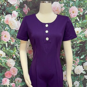 May include: A purple short-sleeved jumpsuit with a round neckline and three silver buttons down the front.