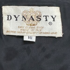 May include: A white tag with black text that reads "DYNASTY" with a crown logo and the text "Dry Clean Only Made in the British Crown Colony of Hong Kong" and a smaller white tag with the number "10" on it.