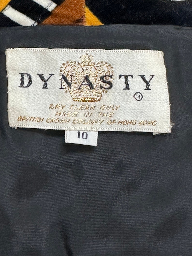 May include: A white tag with black text that reads "DYNASTY" with a crown logo and the text "Dry Clean Only Made in the British Crown Colony of Hong Kong" and a smaller white tag with the number "10" on it.