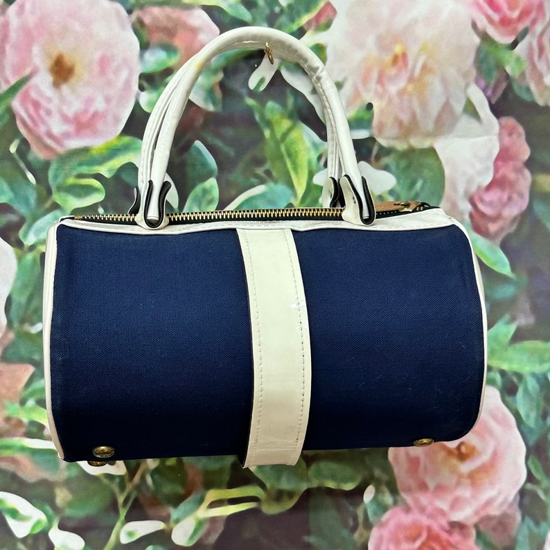 May include: A navy blue and white cylindrical handbag with a white zipper and a white strap.