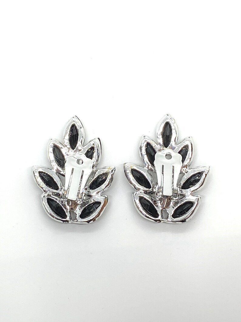 May include: A pair of silver tone clip-on earrings with black leaf-shaped stones.