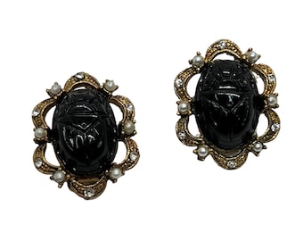 May include: A pair of gold tone earrings with black scarab beetle charms and faux pearl accents.