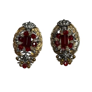 May include: Pair of vintage clip-on earrings. Each earring features a gold-toned, leaf-shaped frame with a central rectangular red stone and smaller red and clear stones. A silver-toned crown sits atop each earring.