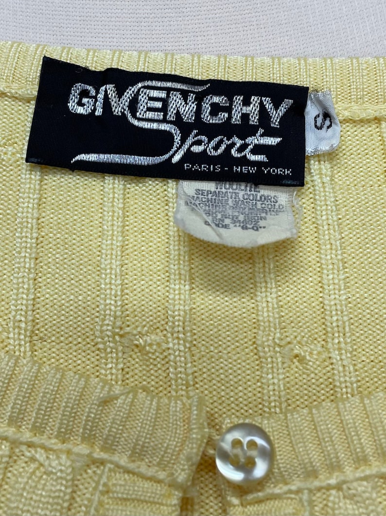 May include: A yellow ribbed knit cardigan with a button closure and a black label that reads "Givenchy Sport Paris - New York".