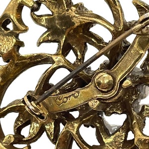 Pu&ograve; includere: Spilla in metallo dorato con un design floreale e una firma Coro sul retro.