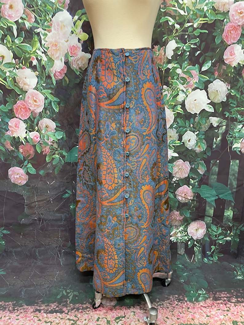 May include: A long blue skirt with a paisley pattern in shades of orange and brown. The skirt has a button-up front closure.