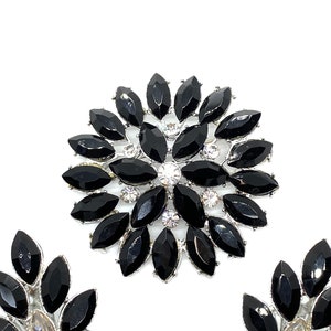 May include: A set of two black and silver brooches with a floral design. The brooches are made of metal and have black rhinestones.