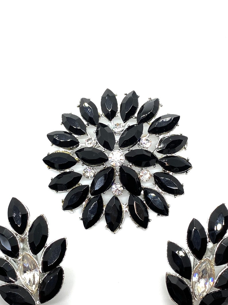May include: A set of two black and silver brooches with a floral design. The brooches are made of metal and have black rhinestones.