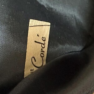 May include: A close-up of a brown fabric label with the text "Le Corde'" printed in black.
