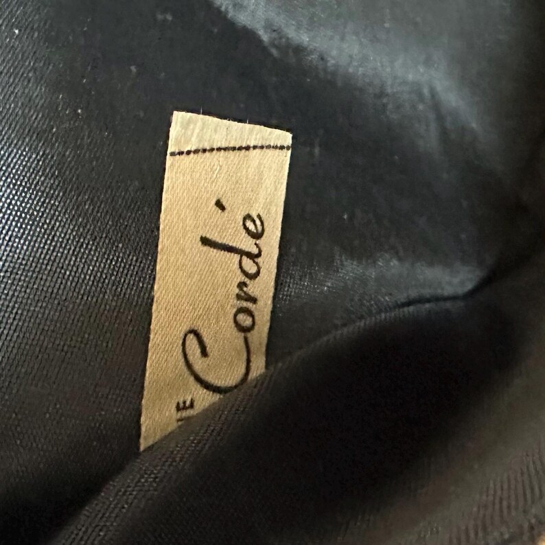 May include: A close-up of a brown fabric label with the text "Le Corde'" printed in black.