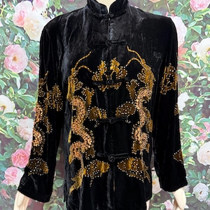 May include: A black velvet long-sleeve jacket featuring a mandarin collar and traditional frog closures. The garment is decorated with gold-toned embroidery and sequins arranged in a dragon motif across the front and down the sleeves.