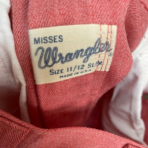May include: A red Wrangler Misses size 11/12 Slim jeans label. The label is white with black text and is sewn onto the inside of the jeans.