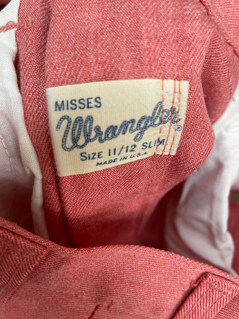 May include: A red Wrangler Misses size 11/12 Slim jeans label. The label is white with black text and is sewn onto the inside of the jeans.