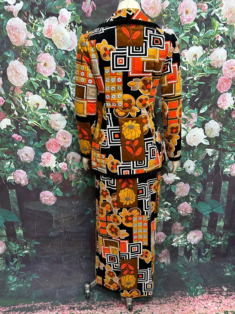 May include: A vintage two-piece suit with a geometric and floral pattern in shades of brown, orange, and black. The jacket has a collar and long sleeves. The skirt is long and has a straight silhouette.