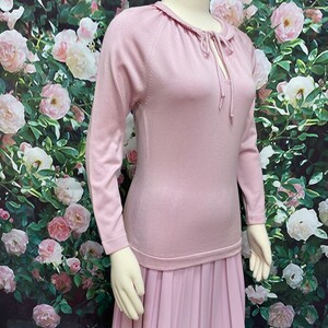 May include: A long, pink dress with a pleated skirt and a fitted bodice. The bodice has a round neckline with a tie detail.