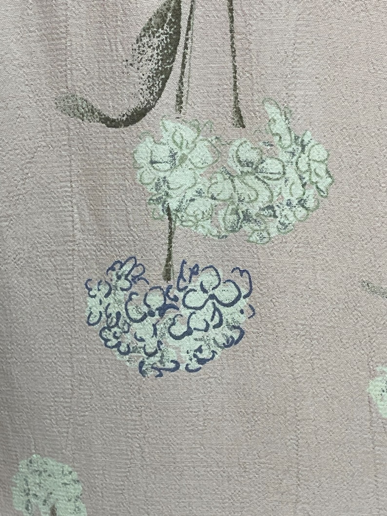 May include: A pale pink fabric with a floral pattern. The flowers are white with a light green outline and a dark blue center.