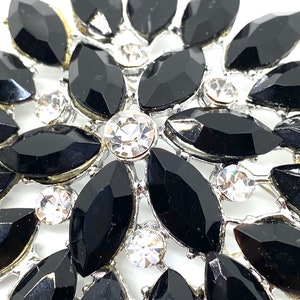May include: A silver brooch with a floral design featuring black and clear rhinestones.