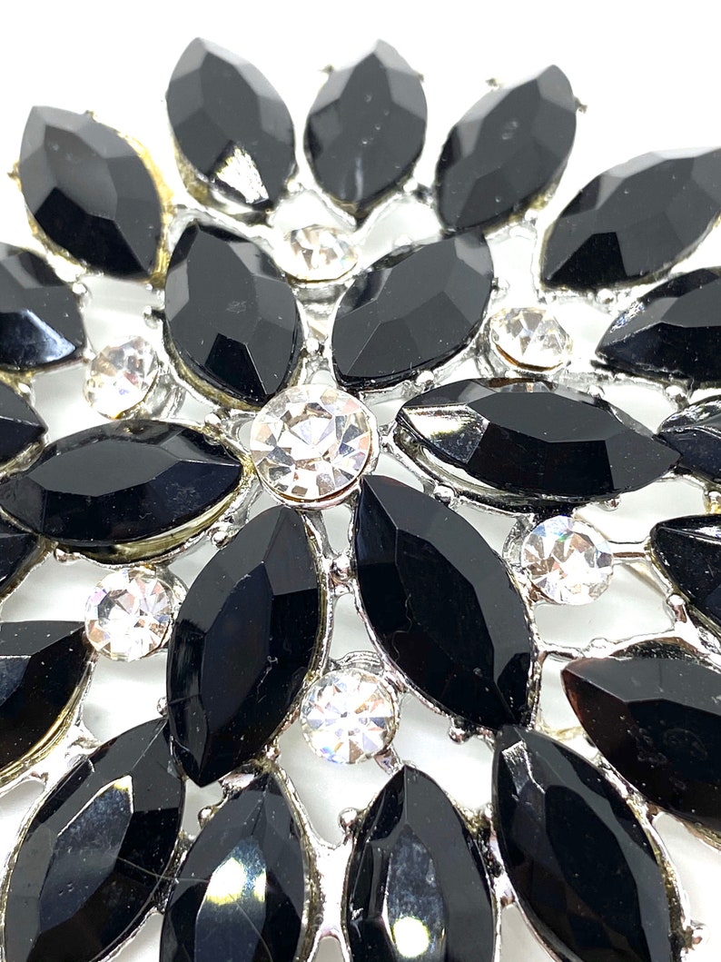 May include: A silver brooch with a floral design featuring black and clear rhinestones.