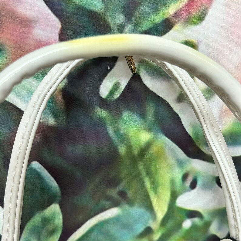 May include: Close-up of the white leather handle of a handbag. The handle is double-stitched and has a slight yellow tint.