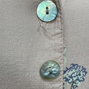 May include: Two pearly white buttons with a light brown thread running through the center holes. The buttons are sewn onto a light pink fabric with a floral pattern.