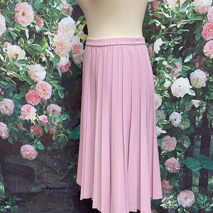 May include: A light pink pleated skirt with a high waist and a knee-length hem.