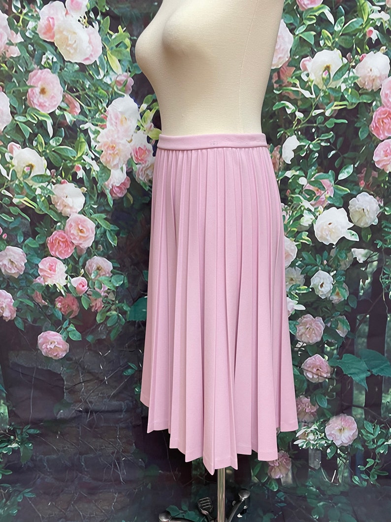 May include: A light pink pleated skirt with a high waist and a knee-length hem.