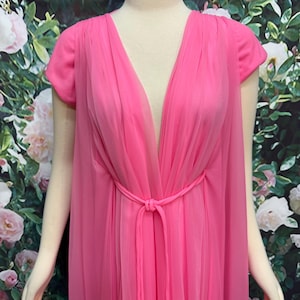 May include: A bright pink floor-length gown featuring a deep V-neckline, short sleeves, and a sheer, layered chiffon overlay. The garment includes a matching fabric tie at the waist, creating a gathered effect across the front bodice.