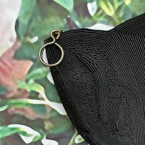 May include: Black woven bag with a gold metal clasp. The bag has a unique textured design.