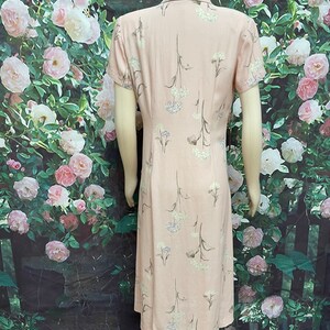 May include: A pink midi dress with a floral print of white flowers and green stems. The dress has a collared neckline and short sleeves.