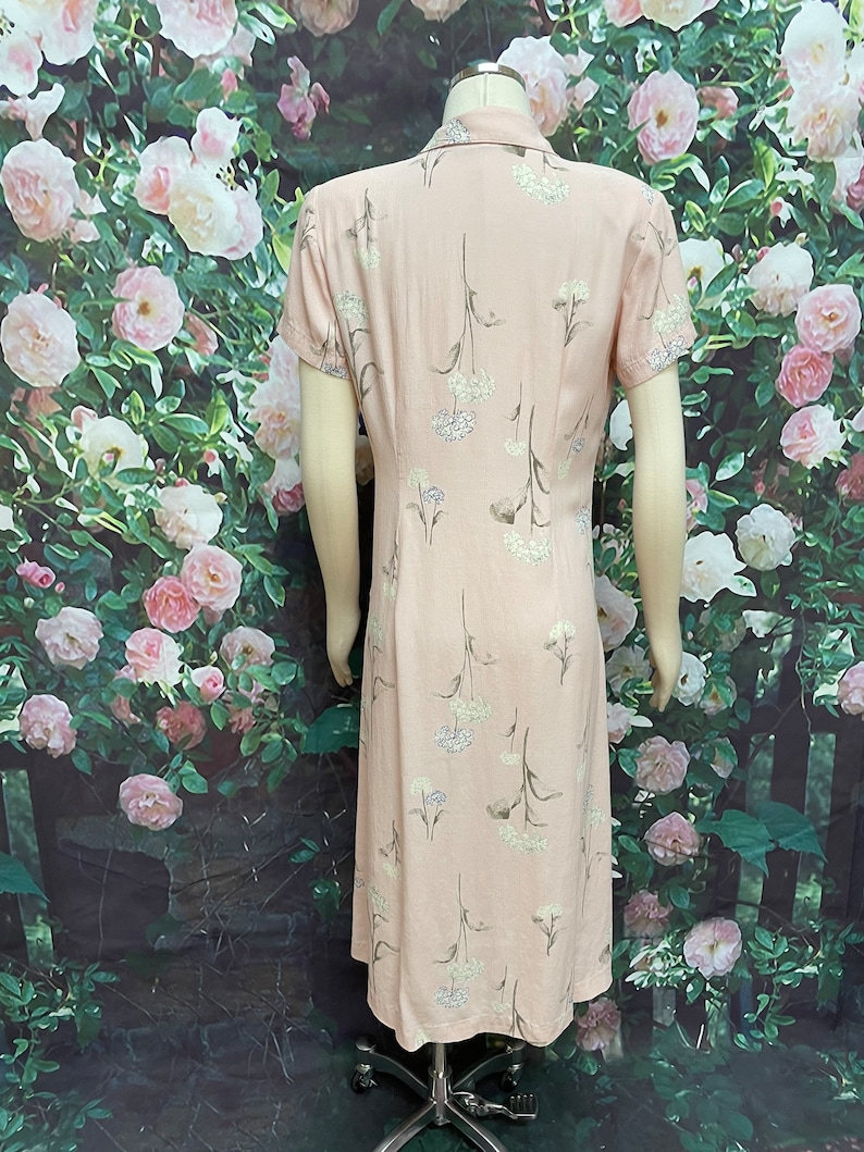 May include: A pink midi dress with a floral print of white flowers and green stems. The dress has a collared neckline and short sleeves.