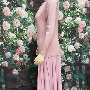 May include: A pink knitted dress with a pleated skirt. The dress has a round neckline and long sleeves.