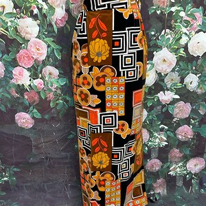 May include: A long black skirt with a geometric and floral print in shades of orange, brown, and white. The skirt has a high waist and a straight silhouette.