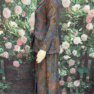 May include: A blue and orange paisley patterned skirt suit. The skirt is long and has a slit up the front. The jacket has a collar and long sleeves.