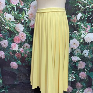 May include: A yellow pleated midi skirt. The skirt is made of a smooth, lightweight fabric and has a simple, classic design.