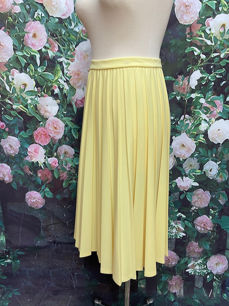 May include: A yellow pleated midi skirt. The skirt is made of a smooth, lightweight fabric and has a simple, classic design.