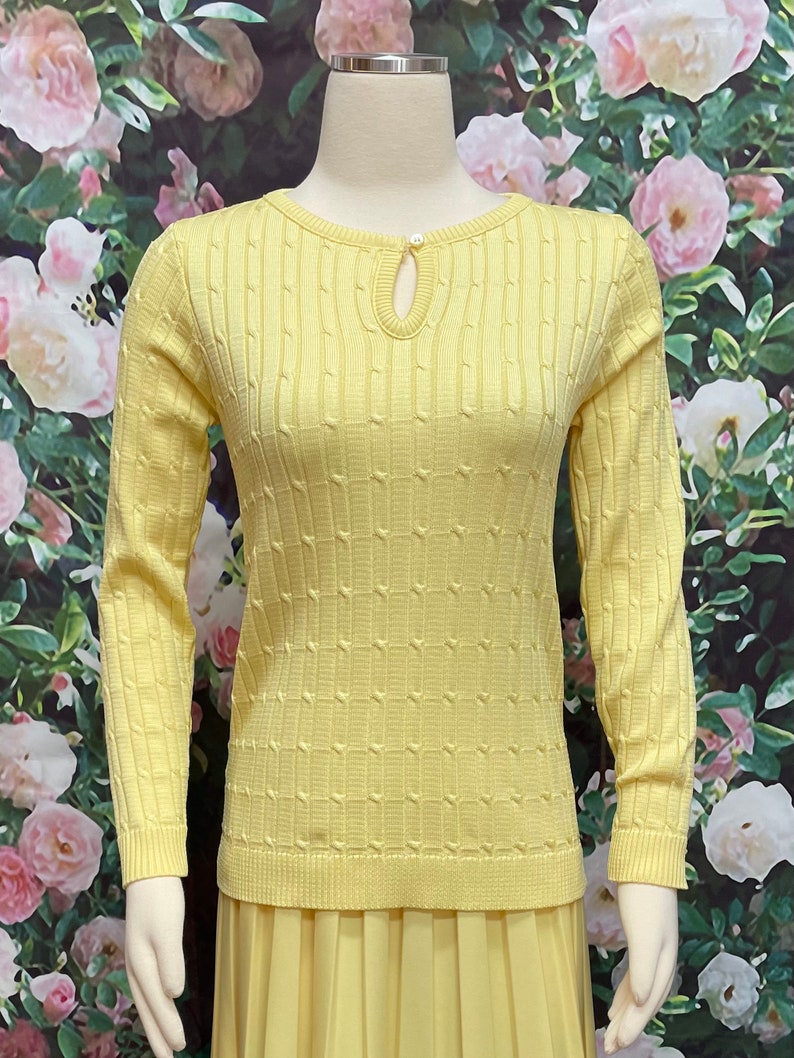 May include: A yellow knitted sweater with a keyhole neckline and a textured pattern. The sweater has long sleeves and a relaxed fit.