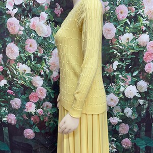 May include: A yellow knitted sweater and matching pleated skirt. The sweater has a cable knit pattern and the skirt is knee-length.