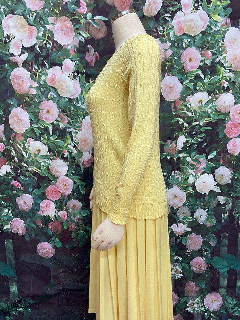 May include: A yellow knitted sweater and matching pleated skirt. The sweater has a cable knit pattern and the skirt is knee-length.