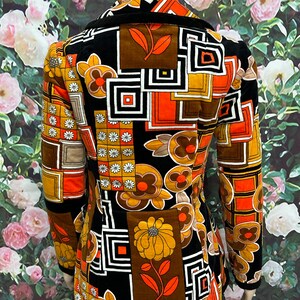 May include: A black velvet jacket with a geometric and floral pattern in shades of orange, brown, and white. The jacket has a collar and long sleeves.