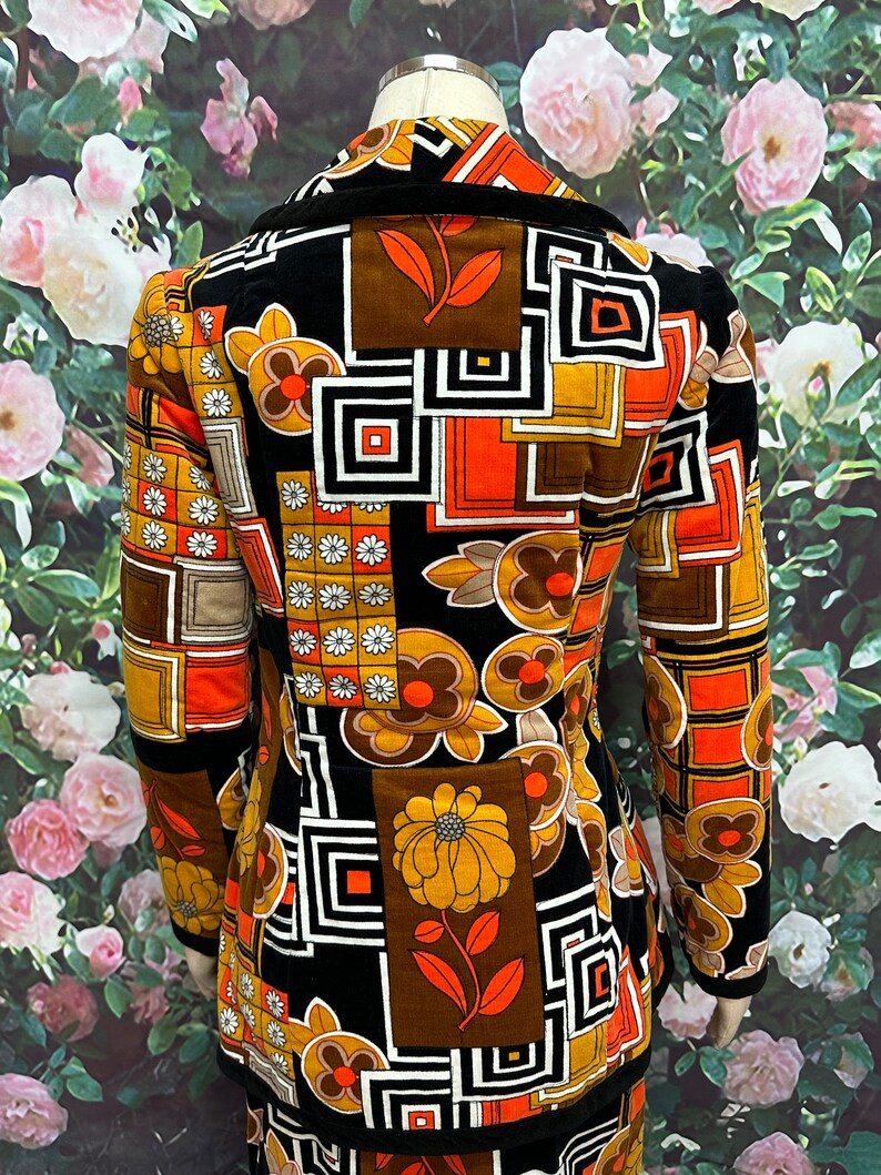 May include: A black velvet jacket with a geometric and floral pattern in shades of orange, brown, and white. The jacket has a collar and long sleeves.