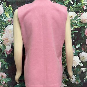 May include: A sleeveless pink vest with a V-neckline. The vest is made of a soft, textured fabric.