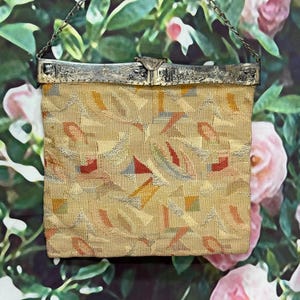 May include: Vintage handbag with a silver-tone frame and chain. The bag features a beige fabric with a colorful geometric pattern in red, yellow, blue, and green. The frame has an ornate design and a clasp closure.