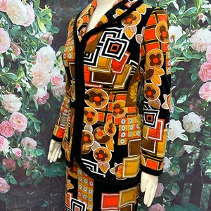 May include: A black and brown vintage skirt suit with a geometric and floral pattern. The suit features a fitted jacket with a collar and a skirt with a straight silhouette.