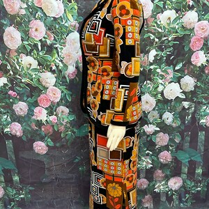 May include: A black velvet skirt suit with a geometric and floral print in orange, brown, and white. The suit features a long skirt with a side slit and a matching jacket with a collar.