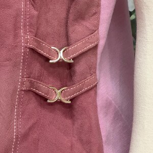 May include: A close-up of a pink suede skirt with two silver buckles. The skirt has a pink and white striped lining.