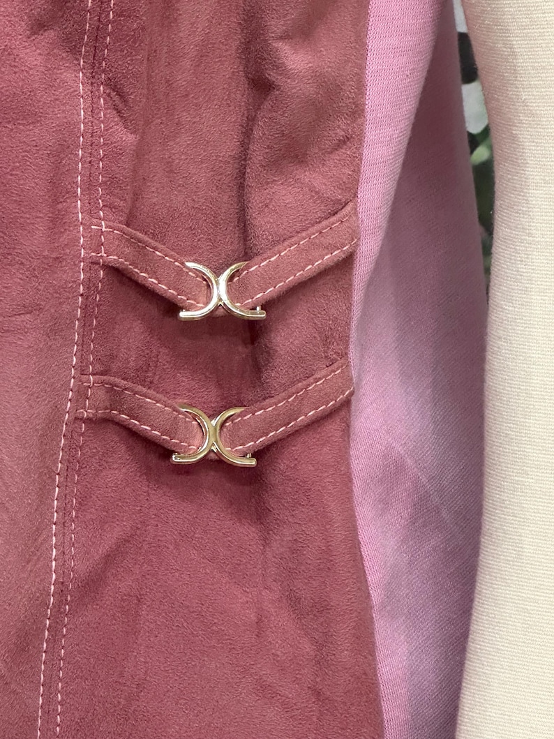 May include: A close-up of a pink suede skirt with two silver buckles. The skirt has a pink and white striped lining.