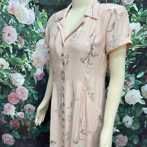 May include: A pink button-down dress with a floral print and a patch pocket. The dress has short sleeves and a collared neckline.