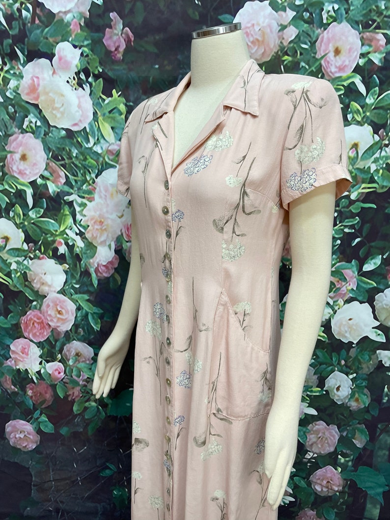 May include: A pink button-down dress with a floral print and a patch pocket. The dress has short sleeves and a collared neckline.