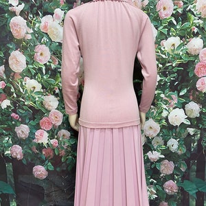 May include: A light pink knitted dress with a pleated skirt. The dress has a round neckline and long sleeves.