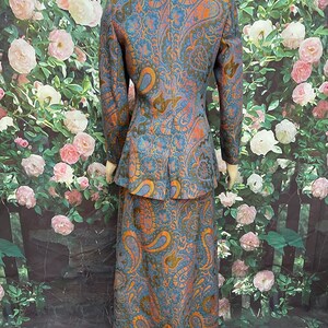 May include: A blue and orange paisley patterned skirt suit. The jacket has a notched collar and long sleeves. The skirt is floor-length.
